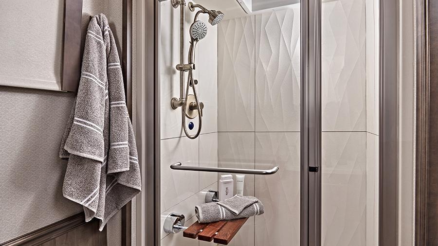 Aspire 44R Shower | The Aspire 44R features a textured porcelain tile shower with a skylight and clear glass shower door, a teak wood shower seat, a fixed shower head and a separate hand-held spray wand. 