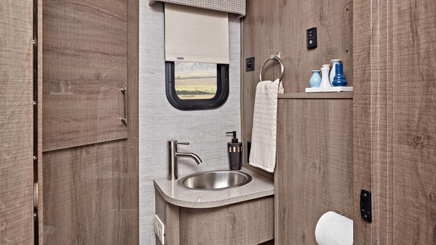 The Entegra Qwest bathroom features a shower with decorative surround and skylight, stainless steel bathroom sink, powered roof vent and porcelain toilet with foot flush. (24N Shown)