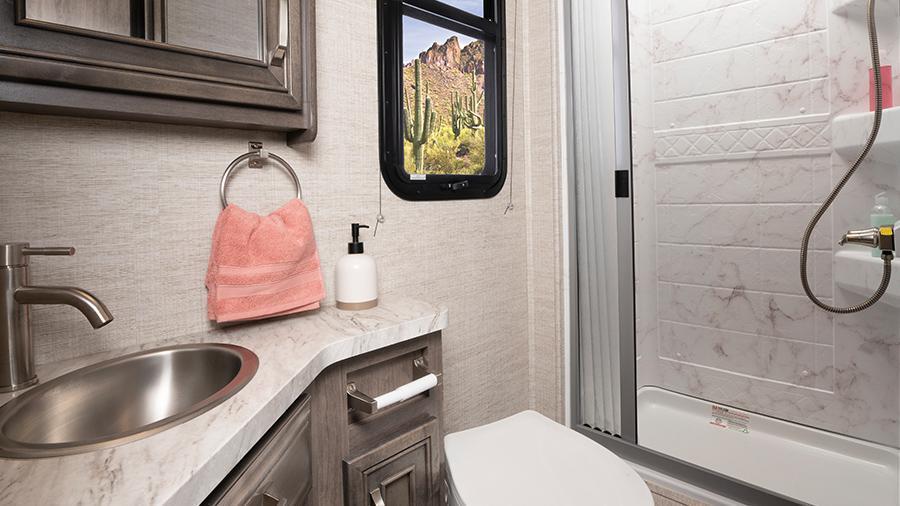 Qwest SE 24L Bathroom | Wash off the day in the Qwest SE 24L bathroom with the shower with decorative surround and skylight, a stainless steel bathroom sink, a toilet with foot flush and a powered roof vent with a wall switch. 