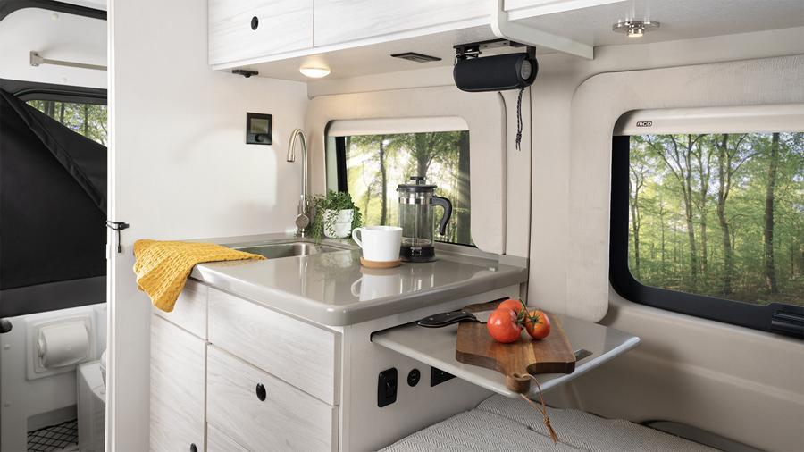 Arc 18C Kitchen | The Arc 18C kitchen has a 3-cubic-foot refrigerator/freezer, a microwave, a portable induction cooktop, a stainless-steel sink with cover and pressed countertops.