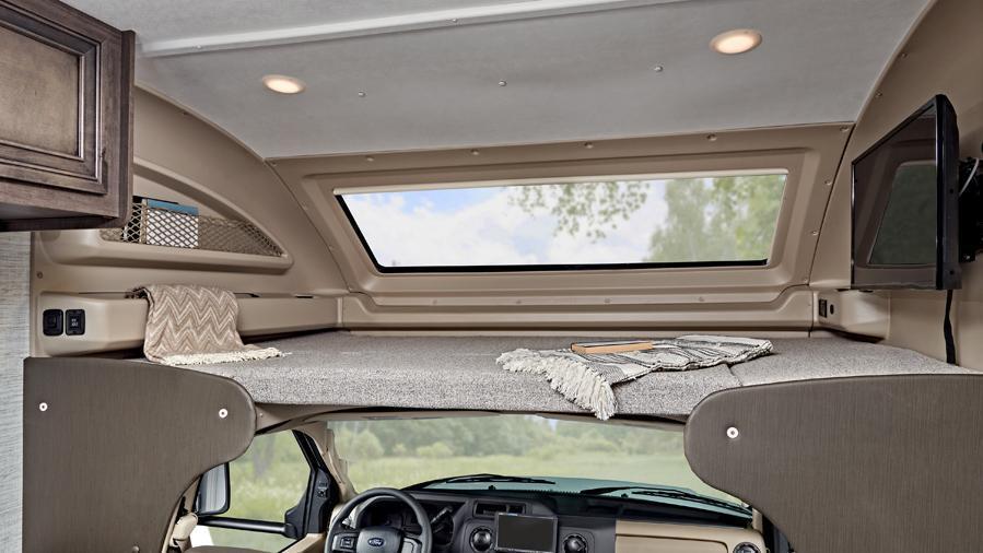 Odyssey SE 22C Overhead Bunk | The overhead bunk in the Odyssey SE 22C has a 750 lb. weight capacity and safety net. Enjoy the view out of the automotive-bonded panoramic window with a power shade in the custom-molded ABS surround in the cab-over area.