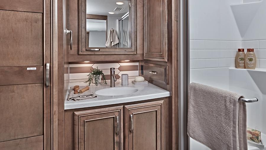 Reatta 39BH Bathroom | The Reatta 39H bathroom has solid-surface countertops with an integrated sink, a one-piece fiberglass shower with a skylight, a Thetford Aqua Magic® toilet with foot flush and Fan-Tastic power exhaust fan with intake. 